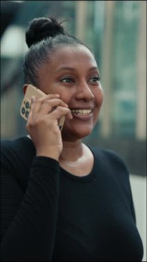 Dikey video. Gülümseyen İş Kadını İş Yeri 'nde Beklerken Müşterilerle Telefonda Konuşuyor. Çok Etnik Kız Telefonla Arıyor ve Telefonunu Çevrimiçi Kullanarak Konuşuyor.