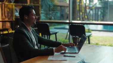 Gülümseyen Hintli adamın portresi şirket ofisinde dizüstü bilgisayarla video konferansına katılıyor. Erkek girişimci, iş arkadaşı olarak internet toplantılarında iş arkadaşlarıyla konuşuyor. İş biçimi