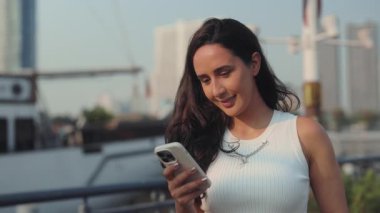 Latin bir kadının portresi şehirdeki akıllı telefondan mesaj okuyor. Esmer kadın, liman yatında cep telefonuyla sosyal medyada sörf yapıyor. İletişim çevrimiçi