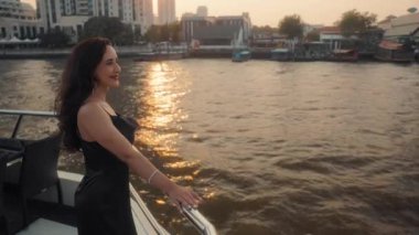 Modern yatta siyah kokteyl elbisesi giyen zarif Latin Amerikalı kadın portresi. Mutlu İspanyol kadın tırabzana eğiliyor. Tatil gezisindeki lüks motorlu tekneye bakıyor.