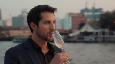 Siyah ceketli mutlu Latin adamın portresi Alacakaranlık 'ta tatilde şampanya yelkenli gemi içiyor. Neşeli İspanyol işadamı Tayland 'da yat gezisini kutluyor.