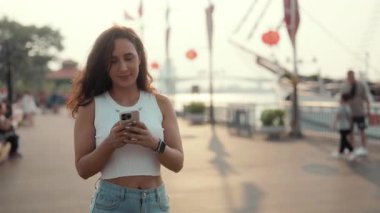 Genç, mutlu Latin bir kadının portresi set boyunca yürürken akıllı telefon tutuyor. Güzel İspanyol kadın cep telefonuyla mesaj gönderiyor. Turistik limandaki modern yatların önünden geçiyor.