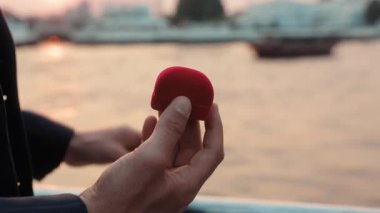 Adamın eli yatta zarif bir nişan yüzüğüyle sakince yaklaşırken kutuyu açıyor. Aşık bir erkek, lüks bir gemide romantik duyguları ve ilişki sahnesini simgeleyen mücevherler taşır.