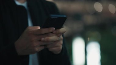 Basit giysiler içinde yüzü olmayan, modern akıllı telefonu siyah çantada tutan, dokunmatik ekranda parmaklarıyla yazan bir insan. Gadget kullanıcısı ışıltılı arka planda bulanık duruyor.