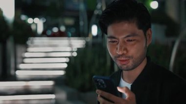 Akıllı telefon tutan heyecanlı Asyalı adamın portresi ve sıkılmış yumrukla el kaldırırken zafer jesti yapıyor. Mutlu insan posta kutusunu kontrol ediyor ve zafer teklifiyle mesaj alıyor.