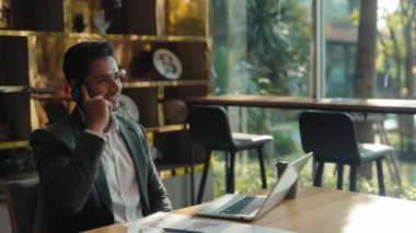 Şemaların yanındaki deneyimli Hintli girişimci portresi ve kapalı alandaki akıllı telefon konuşmaları. Genç serbest çalışan şirket ofisindeki masada oturmuş ticari verileri tartışıyor.