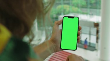 Şık cam bina içinde, boş yeşil ekranlı erkek cep telefonunun yakın çekimi. İçerik yerleştirme veya uygulama arayüzü modellemesi için arkaplan hazır