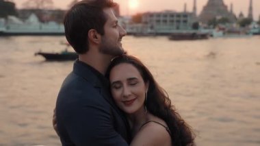 Günbatımında yatta duran Latin Amerikalı çiftlerin nazikçe kucaklaşmalarının portresi. Mutlu İspanyol yeni evli eşler Tayland 'da deniz yolculuğunda aşklarını ifade ederler.