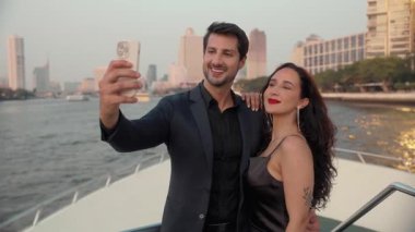 Şenlikli kıyafetler giyen zarif İspanyol çiftin portresi lüks bir yatta selfie çekiyor. Mutlu Latin sevgili motorlu tekne güvertesinde fotoğraf çekiyor. Romantik gezi