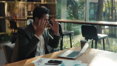 Umutsuz Hintli iş adamının portresi laptopta duygusal olarak el kaldırıyor. Yatırımcı, ortak çalışma odasındaki borsada para kaybetmenin stresini ifade ediyor. İş başarısızlığı