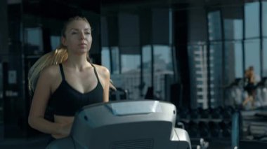 Modern spor kulübünde koşu bandında koşan genç bir kadının portresi. Siyah sutyen giyen atletik bir kadın spor salonunda kardiyo egzersizi yaparak vücut şeklini geliştiriyor.