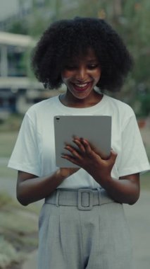 Caddede tablet bilgisayarda çalışan gülümseyen Afrikalı Amerikalı kadının portresi. Mutlu kız öğrenci dışarıdaki dokunmatik cihaza sosyal medya tomarı atıyor. Dikey çekim