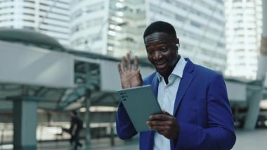 Neşeli Afrikalı Amerikalı girişimci portresi dijital tablet açık havada video görüşmelerine katılıyor. Modern gökdelenlere karşı çevrimiçi toplantıda mutlu iş adamı müşteriyle konuştu