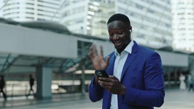 Mutlu Afro-Amerikalı menajerin portresi dışarıda duran akıllı telefondan video çağrısına cevap veriyor. Dost canlısı sakallı iş adamı internette yaptığı toplantıda ortaklarına el sallıyor.