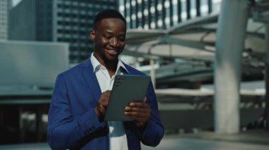 Afro-Amerikalı bir adamın portresi şehir caddesinde tablet yürüyüşleri yapıyor. Gülümseyen genç yönetici dışarıda iş iletişimi sağlayan mobil cihazda e-postaları okuyor.