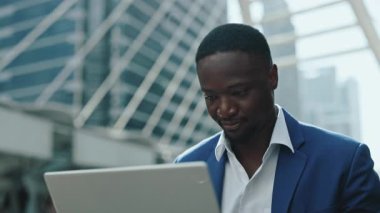 Pozitif Afro-Amerikalı menajerin portresi dizüstü bilgisayarda gökdelene karşı çalışıyor. Mavi ceketli sakallı işadamı şehir merkezindeki defter bilgisayarında internette geziniyor.