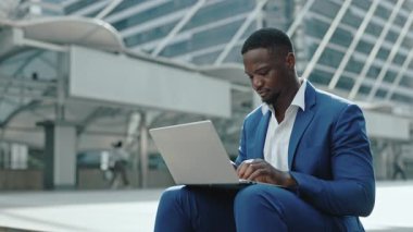 Şirket binasının dışındaki dizüstü bilgisayarda odaklanmış Afro-Amerikan ofis çalışanlarının portresi. Genç işadamı, şehir merkezindeki bir dizüstü bilgisayarla çevrimiçi başlangıç yapıyor.