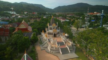 Wat Chalong Tapınağı, güneşli bir günde, yoğun ağaçlarla çevrili dağların bulunduğu yerleşim bölgesinde yer almaktadır. Manevi bir yer Tayland 'ın büyüleyici mimari özelliklerini sunar.