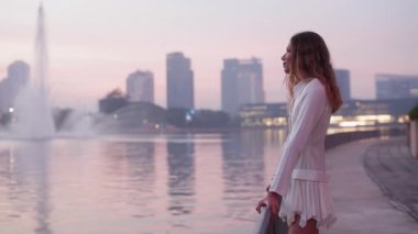 Mini elbiseli tuhaf Asyalı kadın portresi limanda yüksek fıskiyeli jet gözlemliyor. Sarı saçlı pozitif lezbiyen, çitlere yaslanıyor sakin bir akşam nehrine bakıyor.