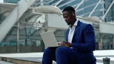 İşitme cihazı olan Afro-Amerikan bir adamın portresi ofis merkezinin yanındaki laptopta çalışıyor. Engelli iş adamı şehir merkezinde oturan dizüstü bilgisayara rapor yazıyor.