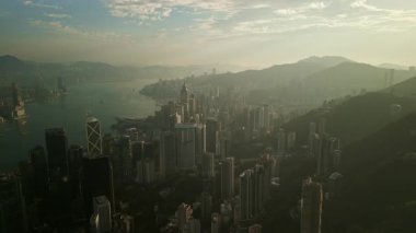 Geniş tepe, adanın ufuk çizgisine ve nazik Victoria liman suyuna doğru gidiyor. Sisli dağlar, ofis kuleleri dolup taşarken şafak vakti sakin Hong Kong 'u oluşturan mahallelerden yükseliyor.