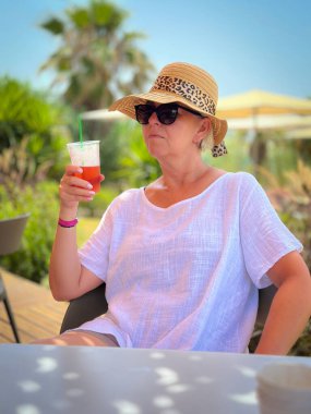 Restoranda bir bardak meyve suyuyla tek başına oturan olgun bir kadının portresi.