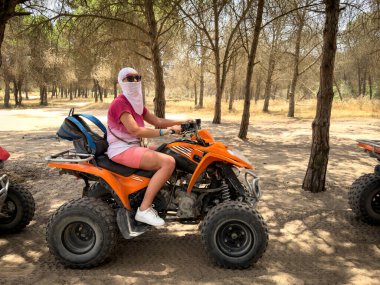 Woman in traditional Arabic headscarf riding an ATV quad bike through a forest landscape in Tunisia.