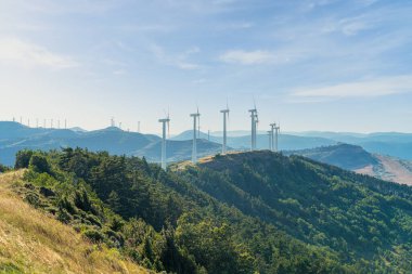 Dağların tepesinde rüzgar türbinlerinin olduğu bir manzara.