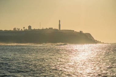 Gün batımında Fas kıyı şeridinin manzarasında deniz feneri olan bir şehir var.