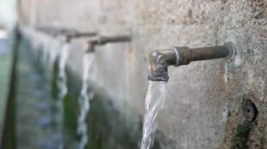 Temiz su, kırsal taştan bir çeşmeden, huzurlu bir açık hava ortamında akar. Bu da doğadaki basit ve ferahlatıcı bir anı gösterir.