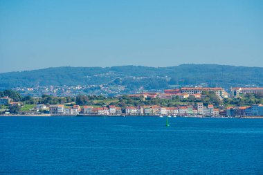 Galiçya 'nın kuzeyindeki Ra de Ferrol' un sakin suları boyunca uzanan sakin Mugardo kıyı kasabası, arka planda geleneksel binalar ve yemyeşil tepeler bulunuyor.