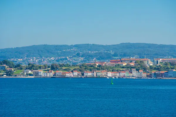 Galiçya 'nın kuzeyindeki Ra de Ferrol' un sakin suları boyunca uzanan sakin Mugardo kıyı kasabası, arka planda geleneksel binalar ve yemyeşil tepeler bulunuyor.