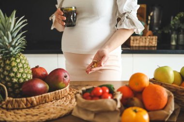 Elinde bir bardak su ve vitamin tutan hamile bir kadın, sağlıklı hamilelik kavramı..