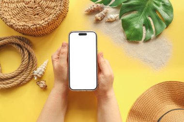 Yaz aksesuarlarının arka planında izole bir ekran olan telefon ellerinizde. Reklamınız için bir yer..