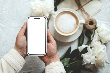 Bir fincan kahvenin arka planında izole bir ekran olan telefon elinde..