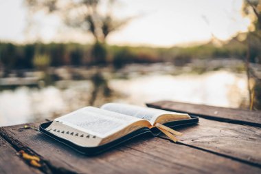 Open Bible on a wooden board near the river. clipart