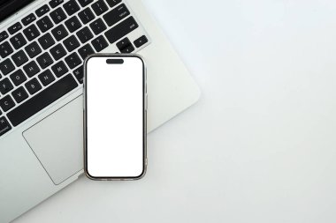 Boş ekranlı akıllı telefon, beyaz renkli masa üzerinde dizüstü bilgisayar ile en az çalışma alanının üst görünümü