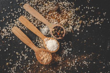 Siyah arka planda farklı baharatlı ahşap kaşıklar, afiş..