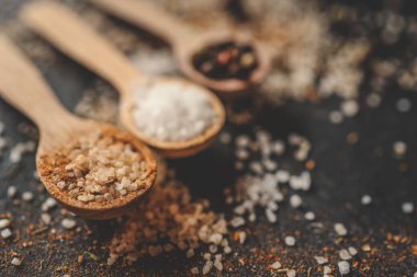 Siyah arka planda farklı baharatlı ahşap kaşıklar, afiş..