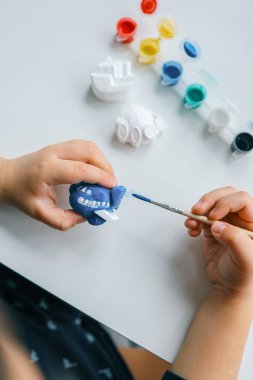 Çocuk alçı figürünü parlak renklerle boyuyor. Çocukların yaratıcılığı kavramı. Anaokulu öğrencisi evde dikiş işi yapıyor..