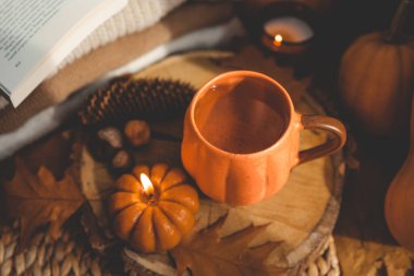 Yanan mum kabağı ve bir fincan çay arka planda bir yığın süveter, sonbahar kompozisyonu.