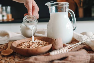 Süt sürahisi, işlenmemiş tam tahılların karışımından yapılmış doğal müsli ile kaseye süt döküyor..