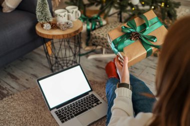 Noel ağacının yanında elinde hediye kutusu olan bir kız, dizüstü bilgisayarında izole edilmiş bir ekran..