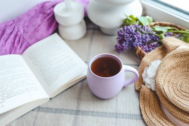Bir fincan çay, hasır şapka ve leylak sepeti, bahar durgun hayat.