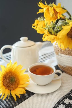 A cup of tea and a teapot with a candle on a table with sunflowers, tea time, aesthetics