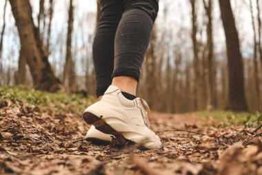 Ormanda koşan bir kadının bacaklarını kapatın. Spor ayakkabılar. Arka planda ağaçlar ve yapraklar var. Aktif ve sağlıklı yaşam tarzı kavramı.