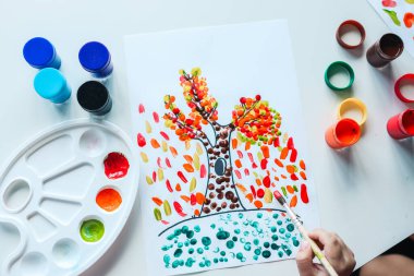 Çocuk sonbahar yapraklarıyla bir ağaç boyuyor, sanat konsepti.