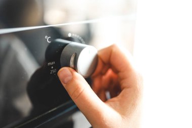 Modern mutfakta kadınlar fırını açıyor. Kadın elinin ve fırın düğmesinin görüntüsünü kapat.