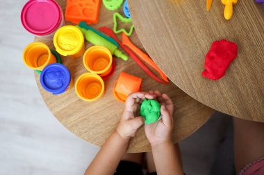 Bebek elleri beyaz masa arkasında kırmızı modelleme kilini tutuyor ve yoğuruyor. - Yakın çekim. Bebek gelişimi. Farklı rengarenk şekiller yapmak için malzeme hazırlanıyor.