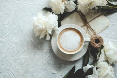 Yaz kompozisyonu üst görünümü. Bir fincan kahve, şakayık ve gri arka planda klasik mektuplar..